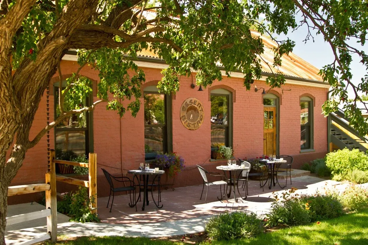Patrons dine outdoors at Moab's Sunset Grill overlooking a town and mountains at dusk.