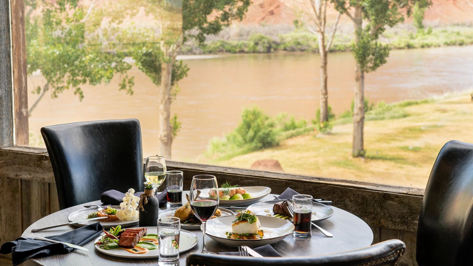 Table set for dining with food and drinks, overlooking a river through a window.