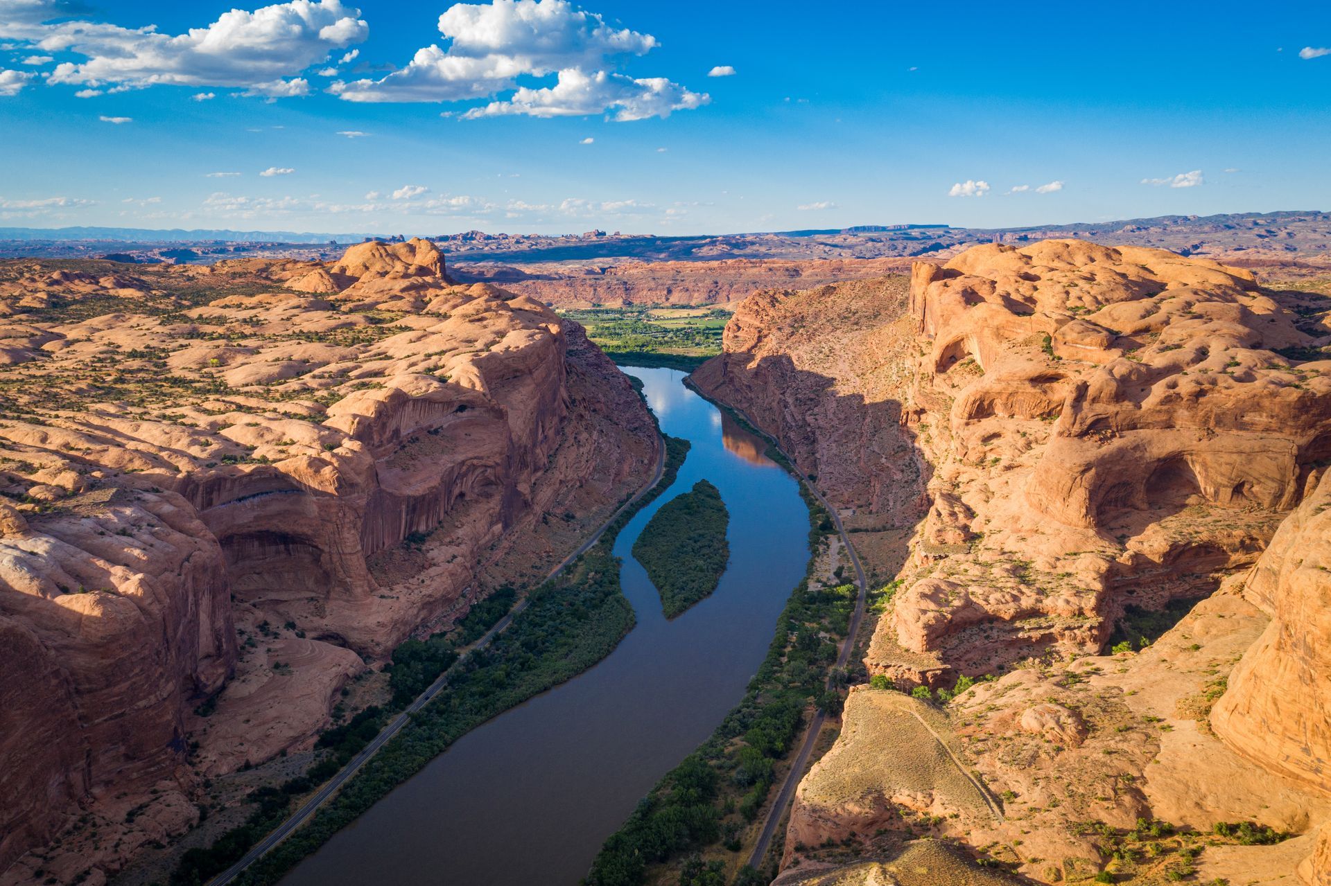 Red rock canyon with Colorado River from above, green vegetation, and blue sky.