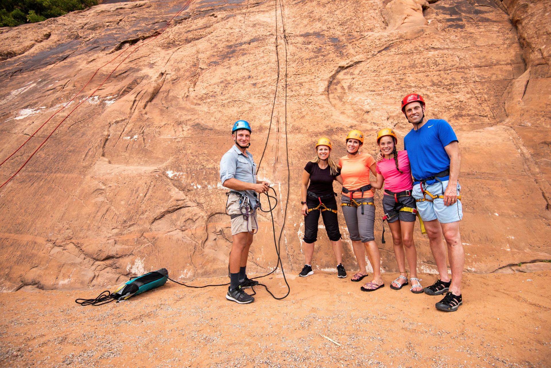 Group of people in climbing gear pose in front of a rock face with ropes.