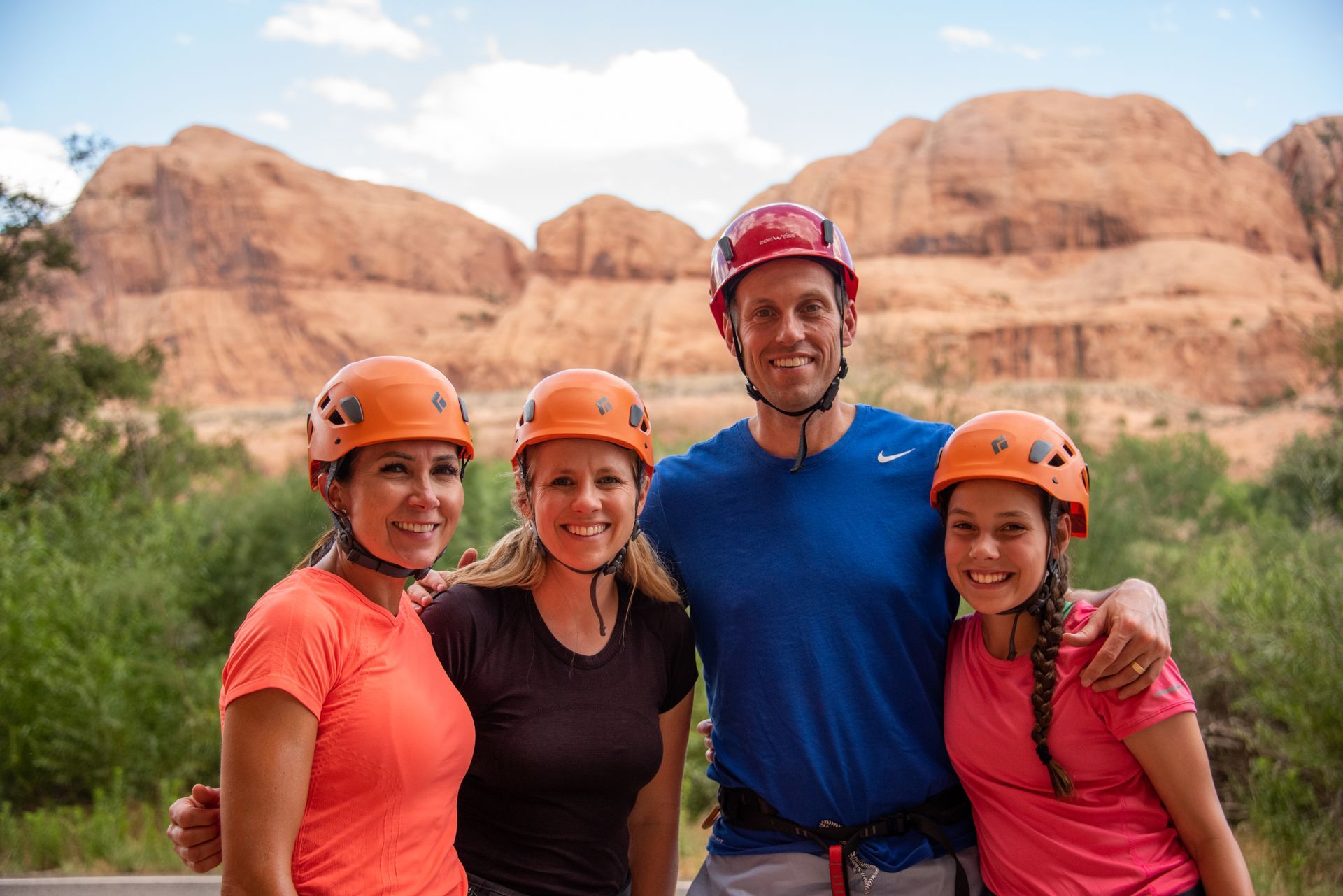 Four people in helmets pose in front of red rock formations in climbing helmets.