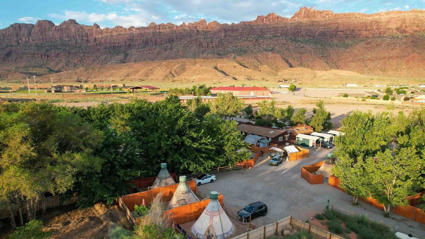 Campground with teepees and cars, red rock mountains in background.