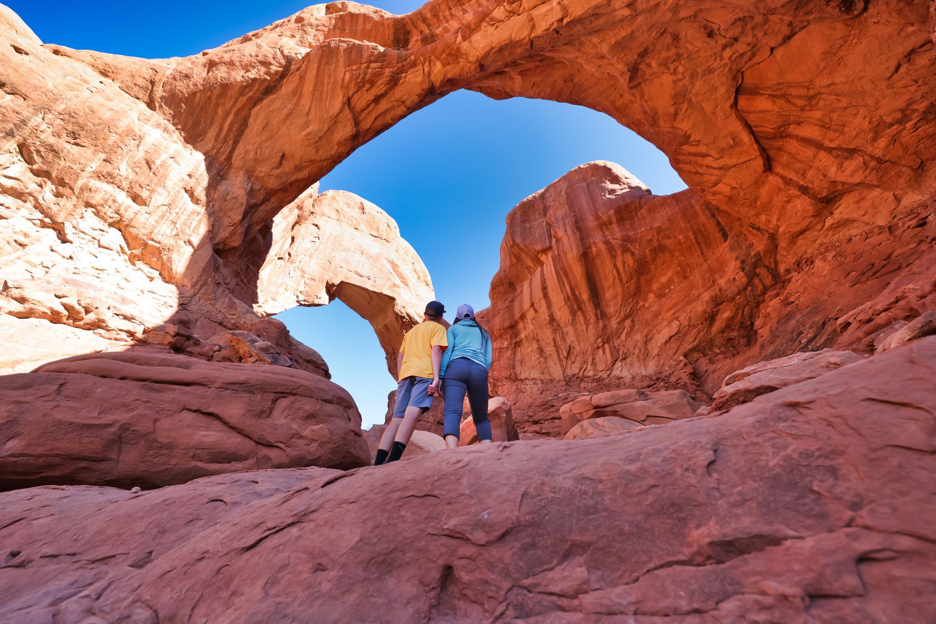 A mother and son look up at Double Arch in Arches National Park.