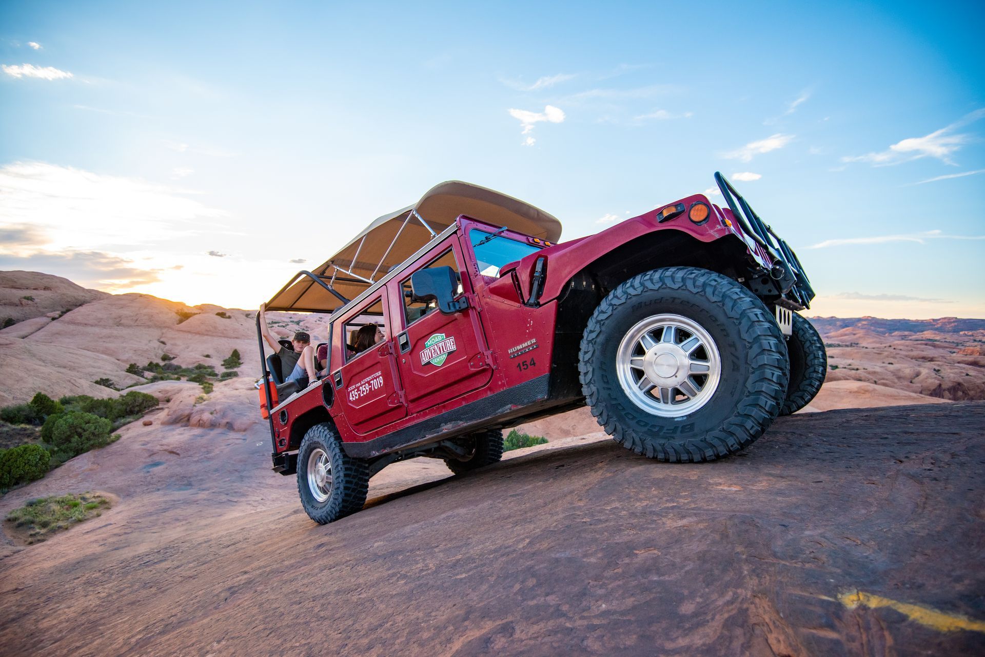 Red off-road vehicle climbs a rocky slope at sunset.