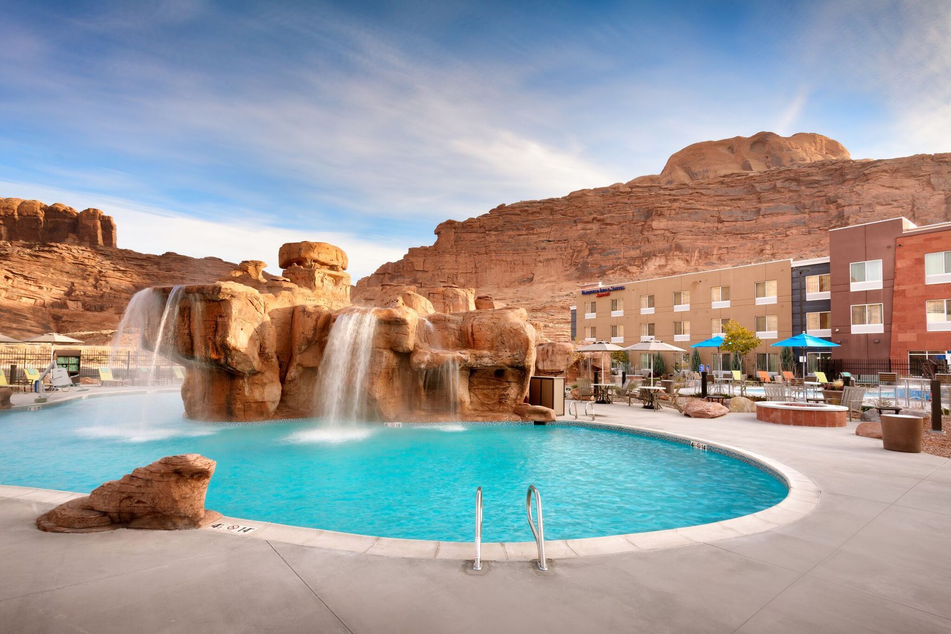 Pool with waterfalls and hotel, set against a red rock mountain under a blue sky.