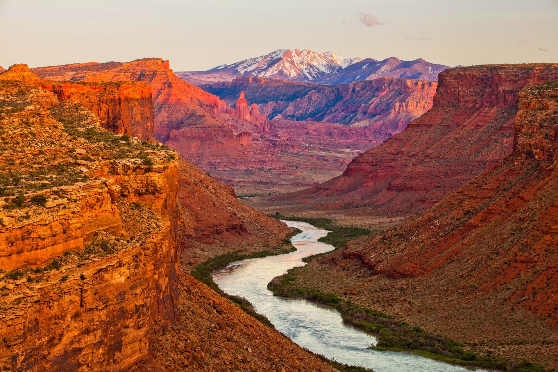 Sunset over a winding river in a red-rock canyon with distant snowcapped mountains