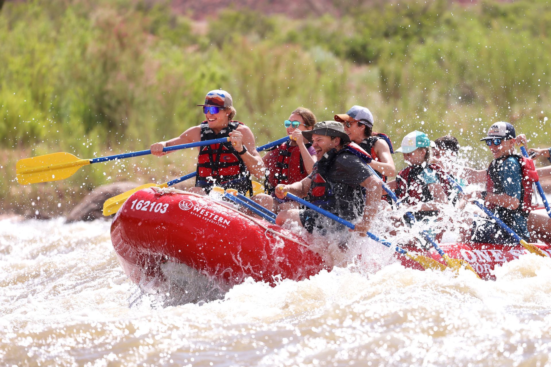 Family raftingon the Colorado River in a red paddleboat through rapids.