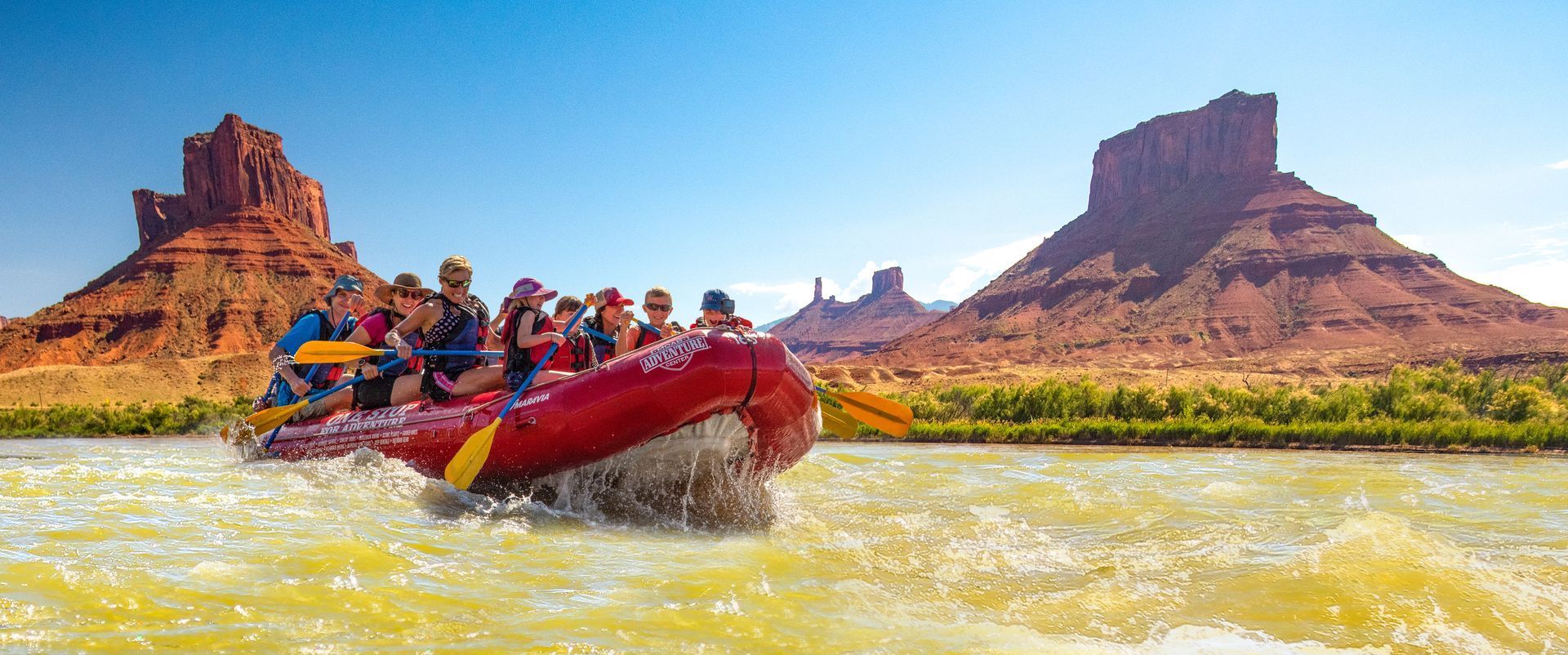 Rafting on a river with red rock formations in the background on a sunny day.
