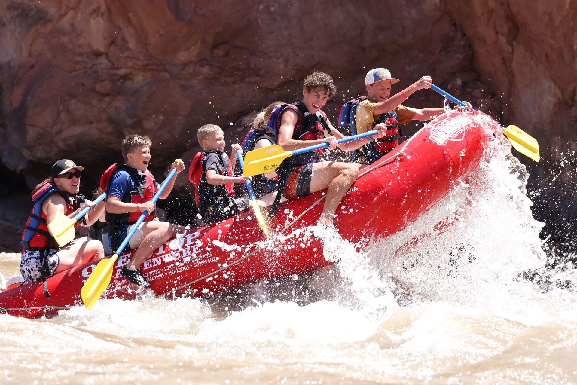 White water rafting, group of young people on red raft, paddling through rapids, splashing water.