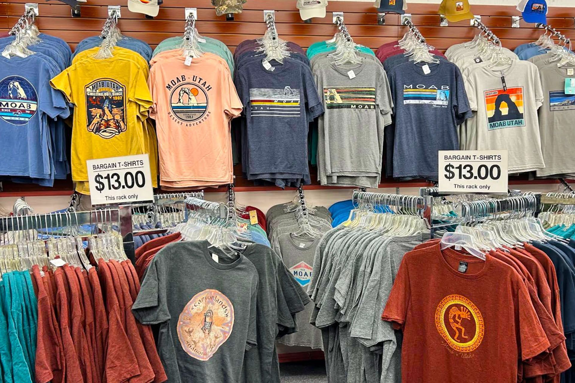 T-shirts in various colors with graphic designs displayed in a store, priced at $13.