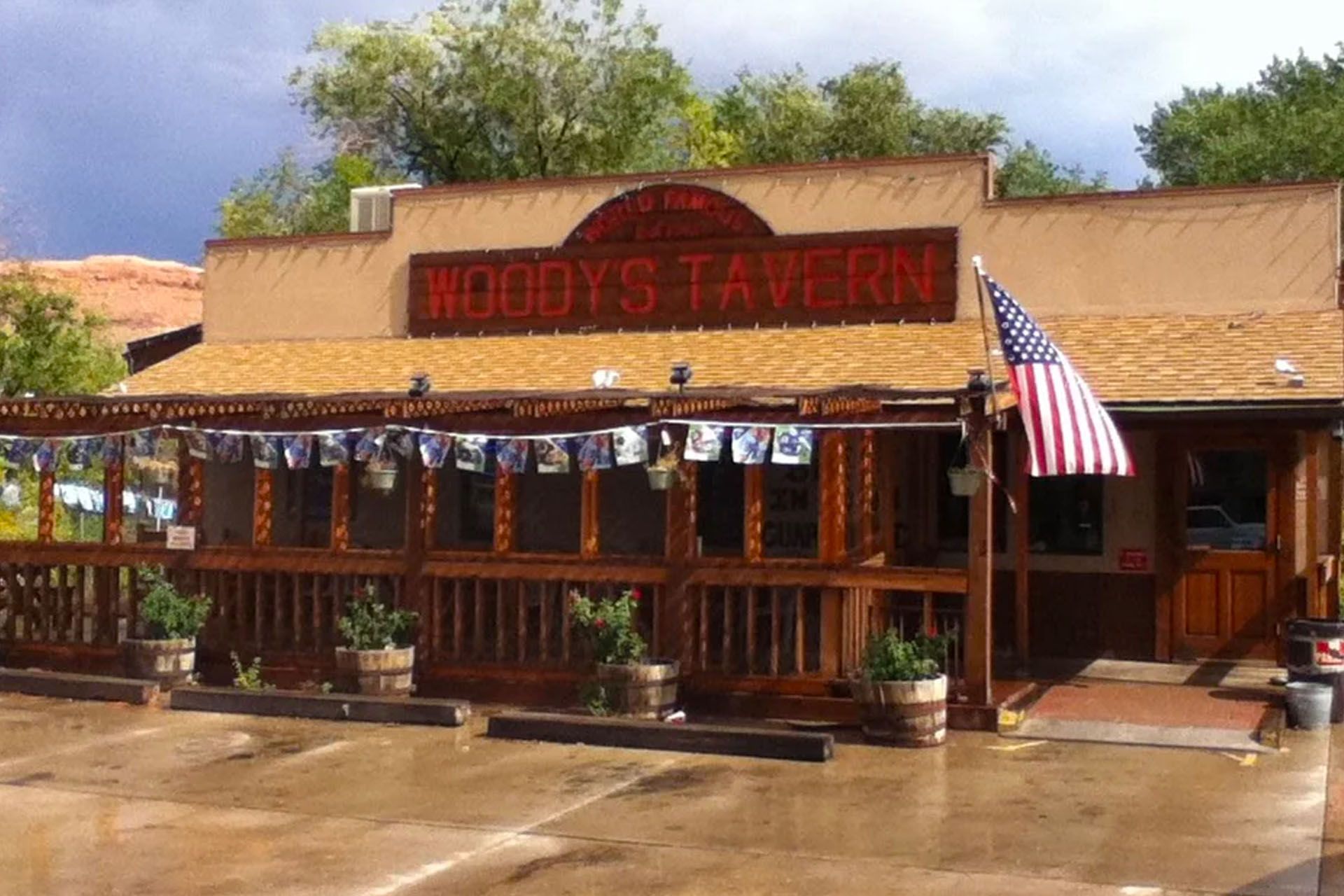 Woody's Tavern with American flag, brown building, and outdoor seating.