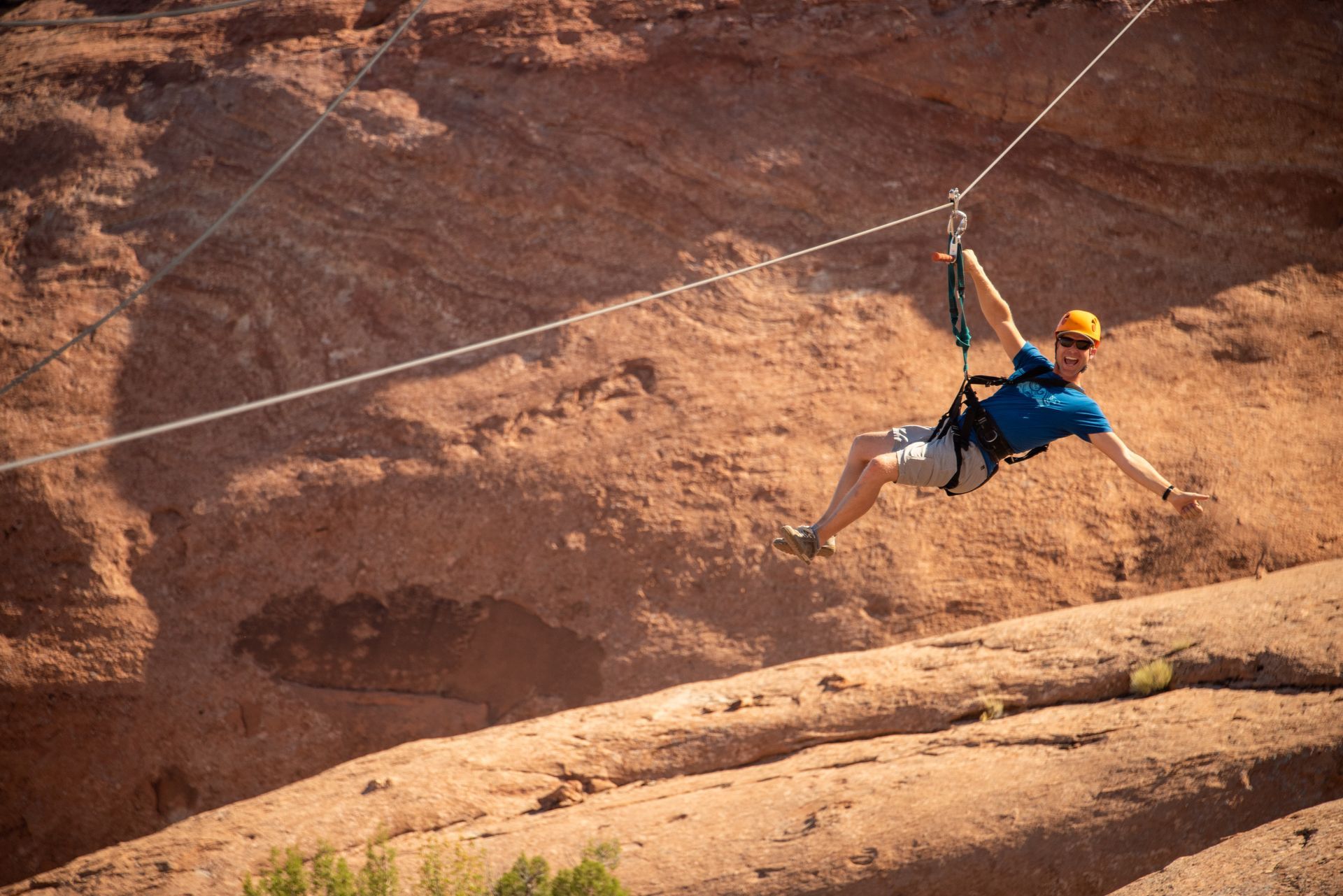A smiling man ziplining over a red rock canyon in Moab, Utah.