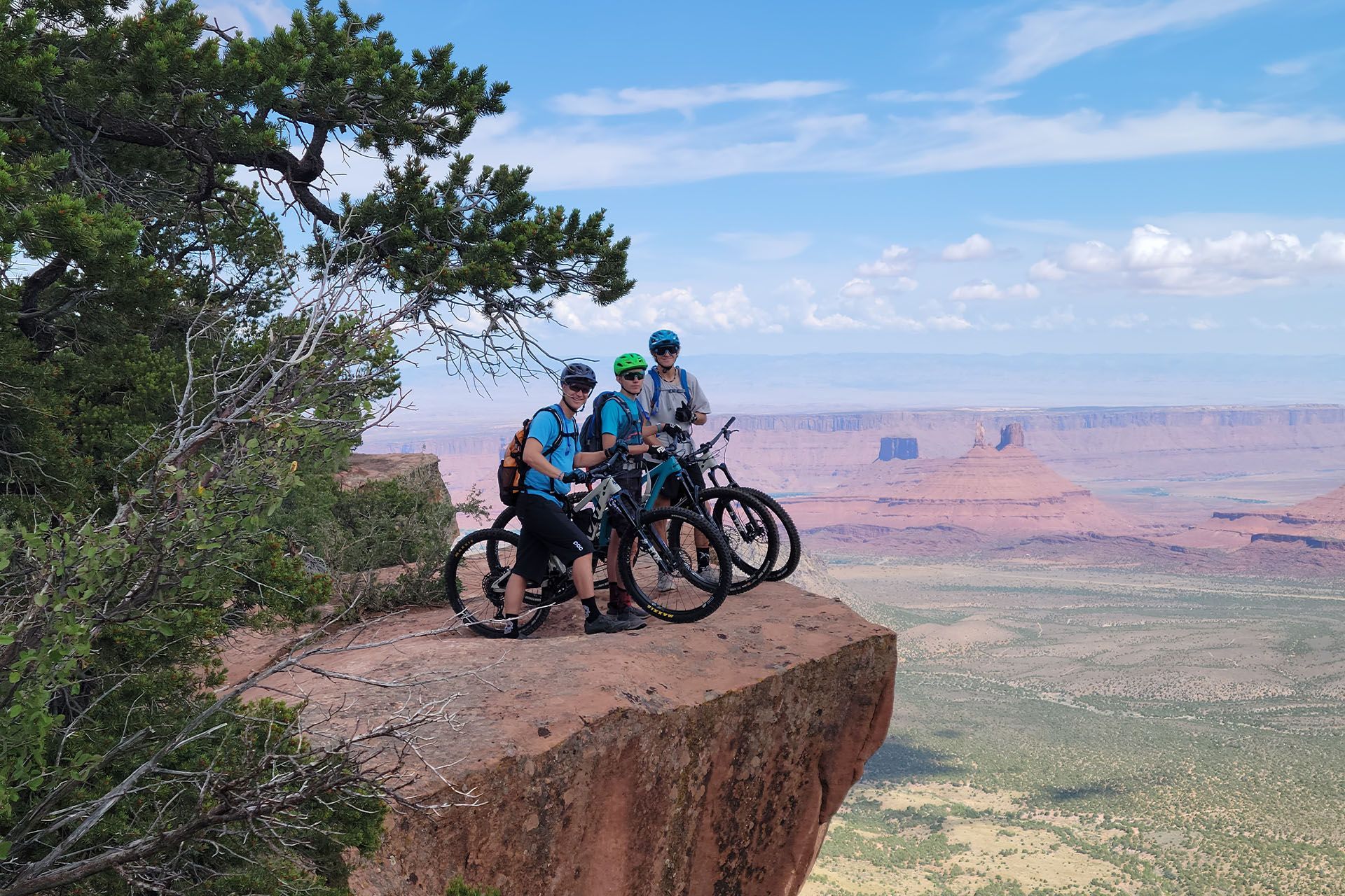 Three mountain bikers on Porcupine Rim overlooking a vast desert valley.