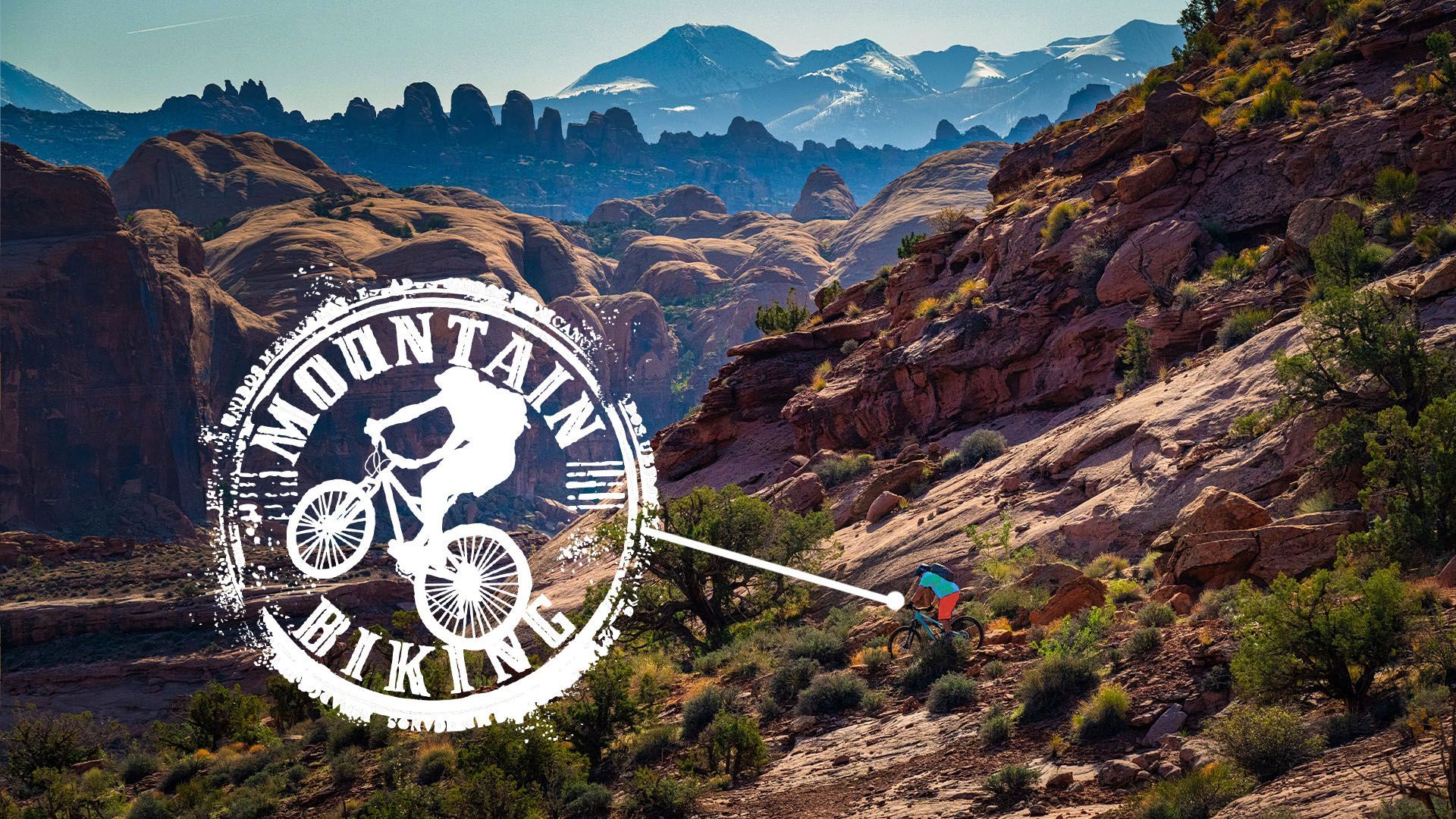 Mountain biker on trail in rocky terrain, mountains in background. Logo overlay reads 