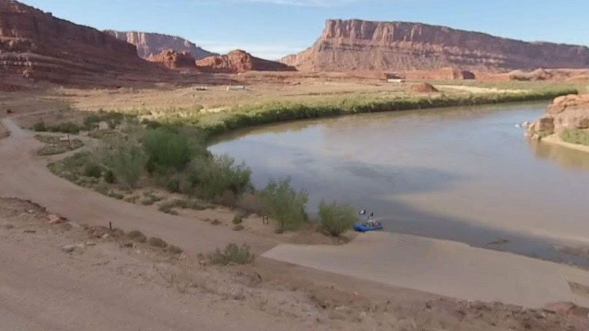 Sandy riverbank with raft on a bend in the river, red rock cliffs in the background.