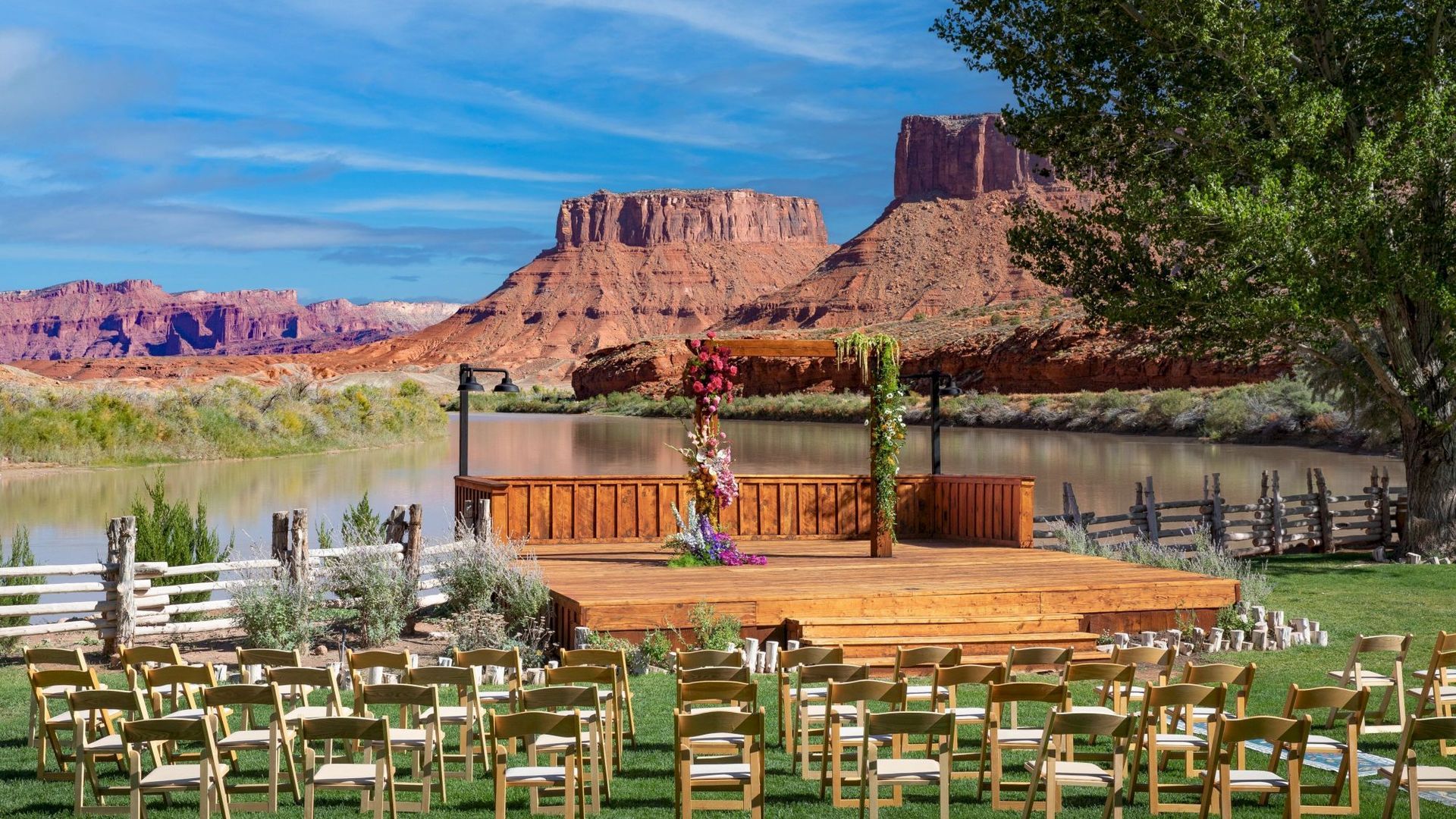 Wedding ceremony setup overlooking a river and red rock formations. Wooden stage, chairs, and decorations.