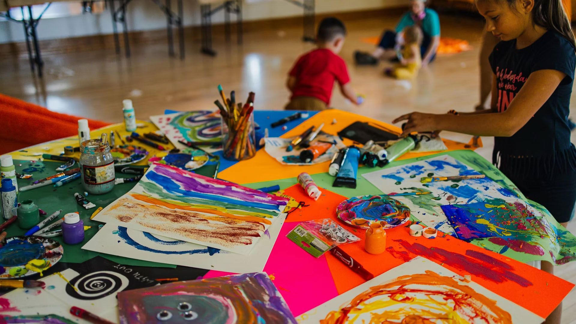 Children at an art table, painting with colorful paints and markers.