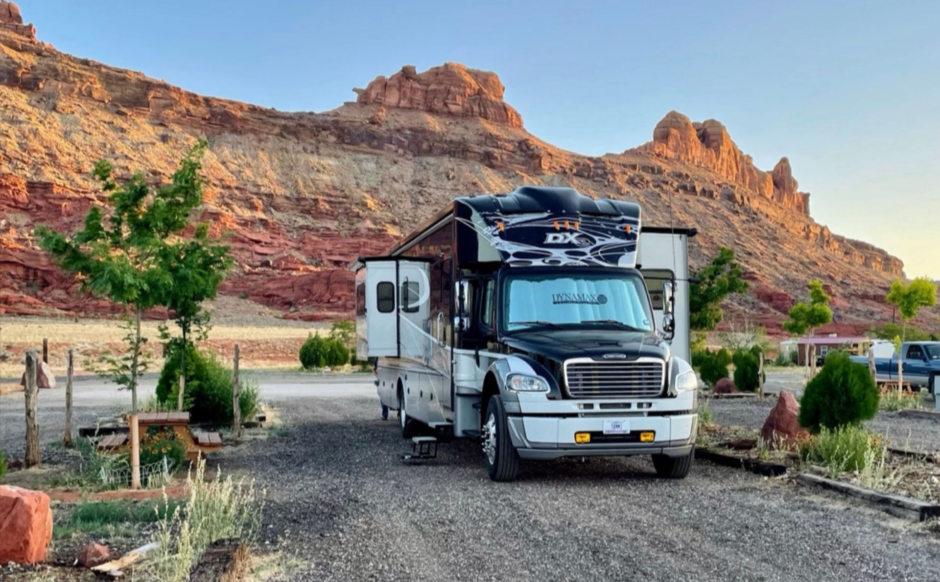 RV parked at a campsite with red rock cliffs in the background at sunset.