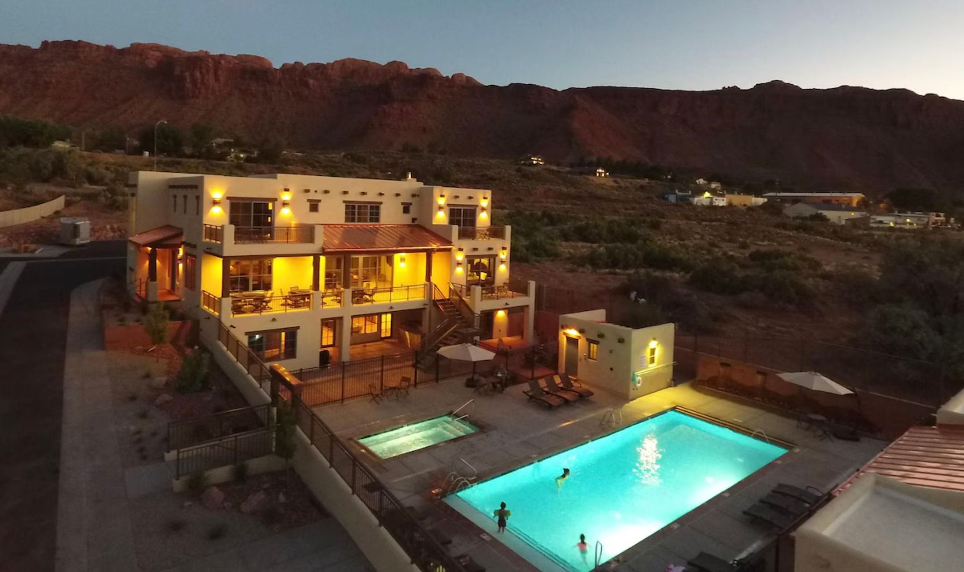 Slickrock lodge vacation rental from abovve with hot tub and pool in evening light with house and pool lights on.