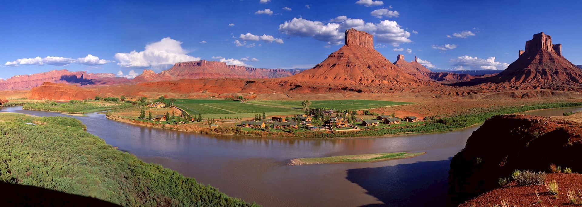 Panoramic view of a river winding through a desert landscape with red rock formations under a blue sky.