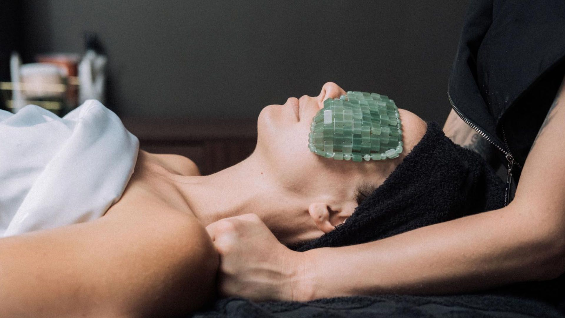 A woman gets a massage with a green eye mask over her face.