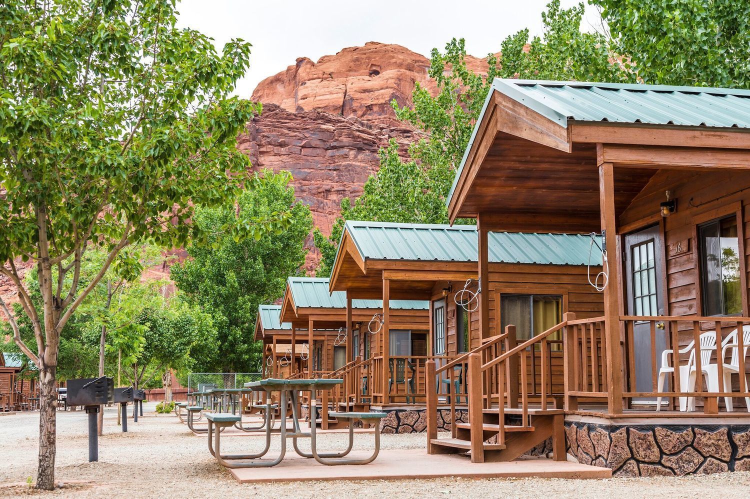 Glamping tent with wooden chairs on a deck, surrounded by plants, outdoors.