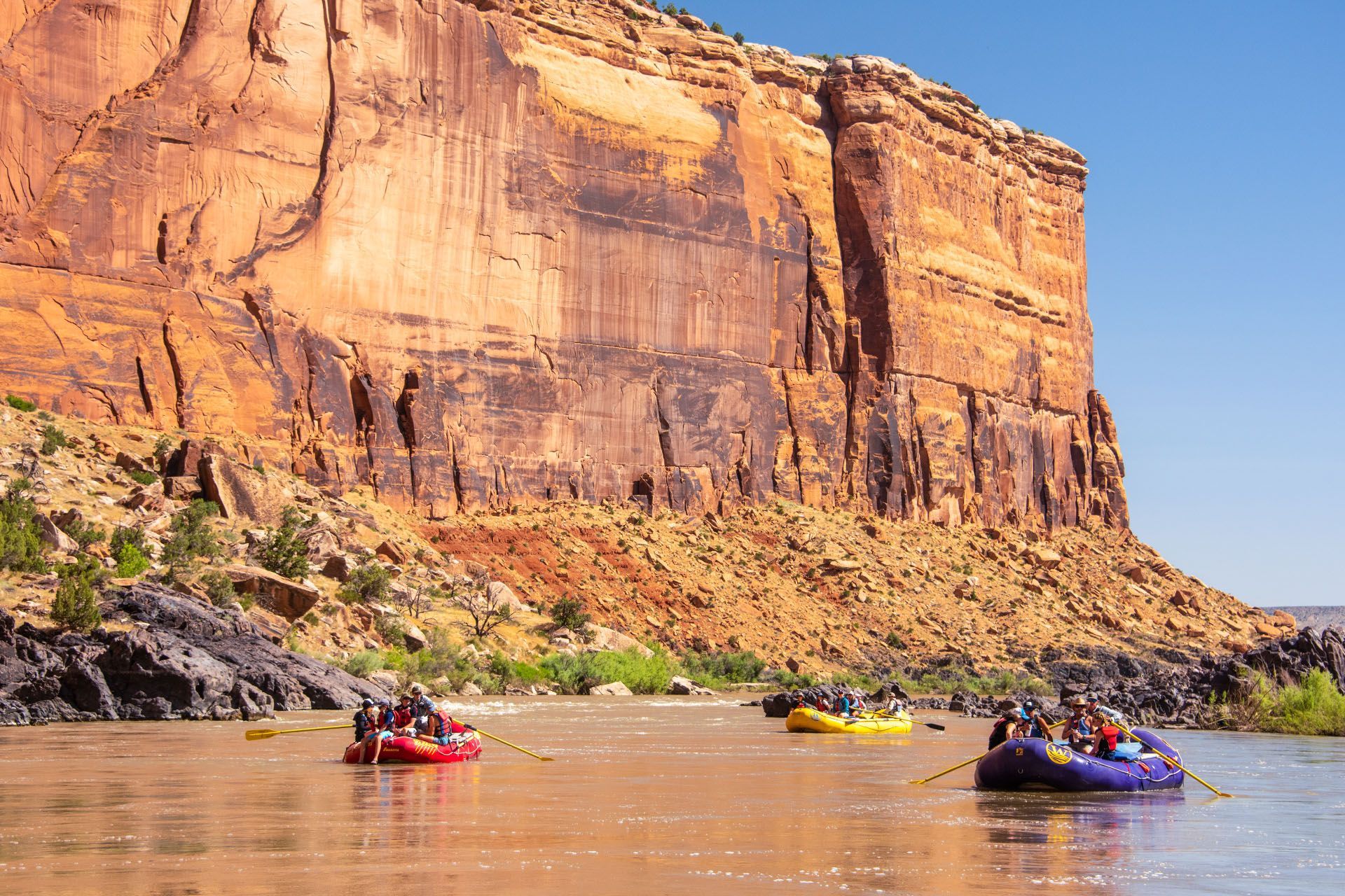 Rafts float on a calm section of Westwater Canyon with tall cliffs in the background.