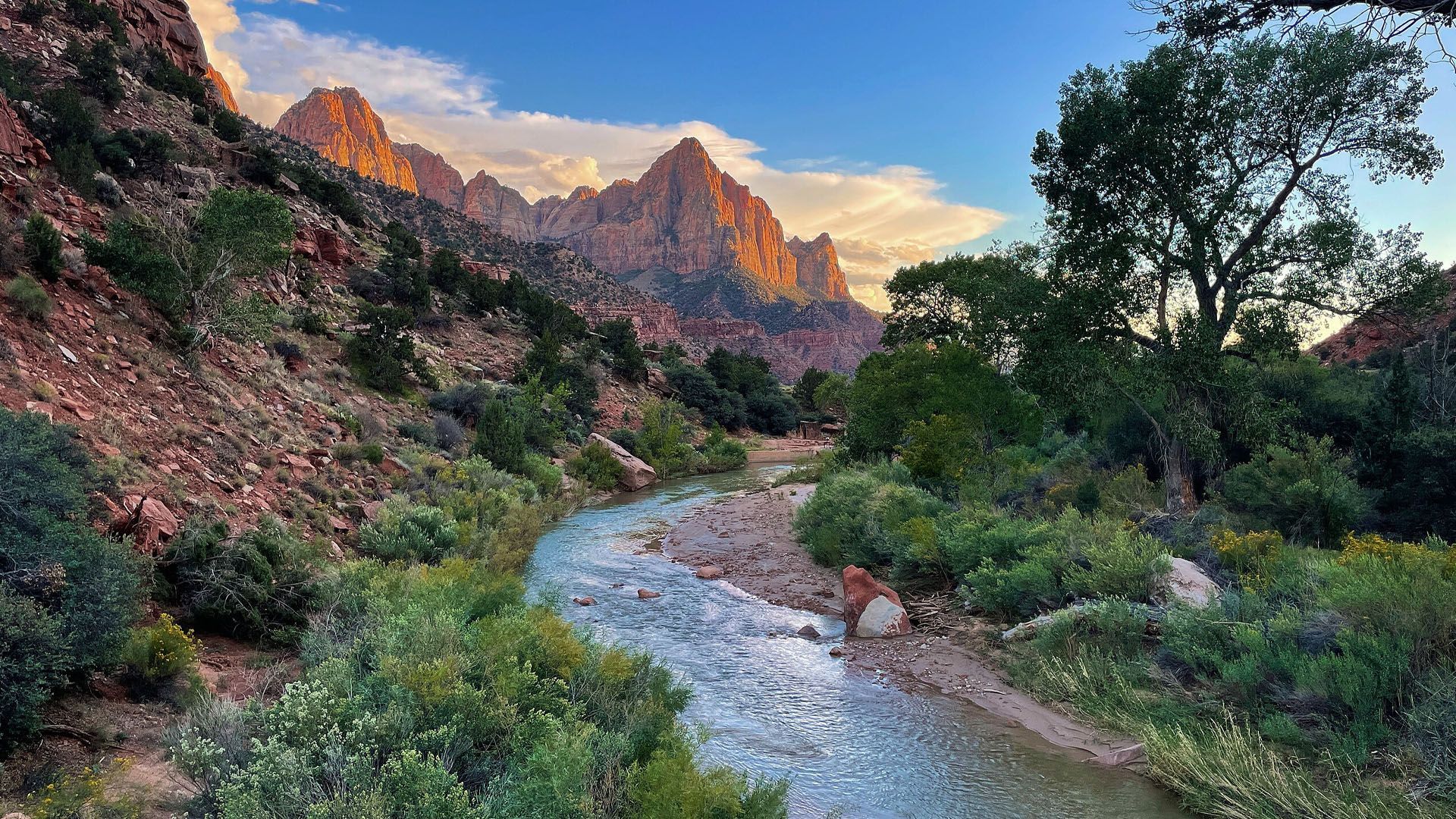 River flowing through a canyon with mountains and green vegetation at sunset.