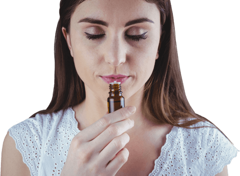 Woman with closed eyes sniffs a small brown bottle, likely essential oils, against a white background.