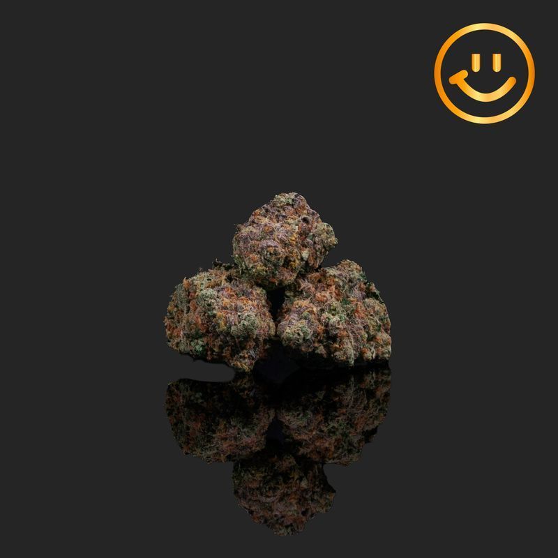 Three cannabis buds with purple and green hues, reflected on a black surface, with a smiling face emoji in the corner.