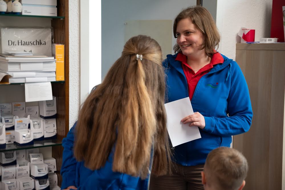 Eine Frau in einer blauen Jacke spricht mit zwei Mädchen und einem Jungen.