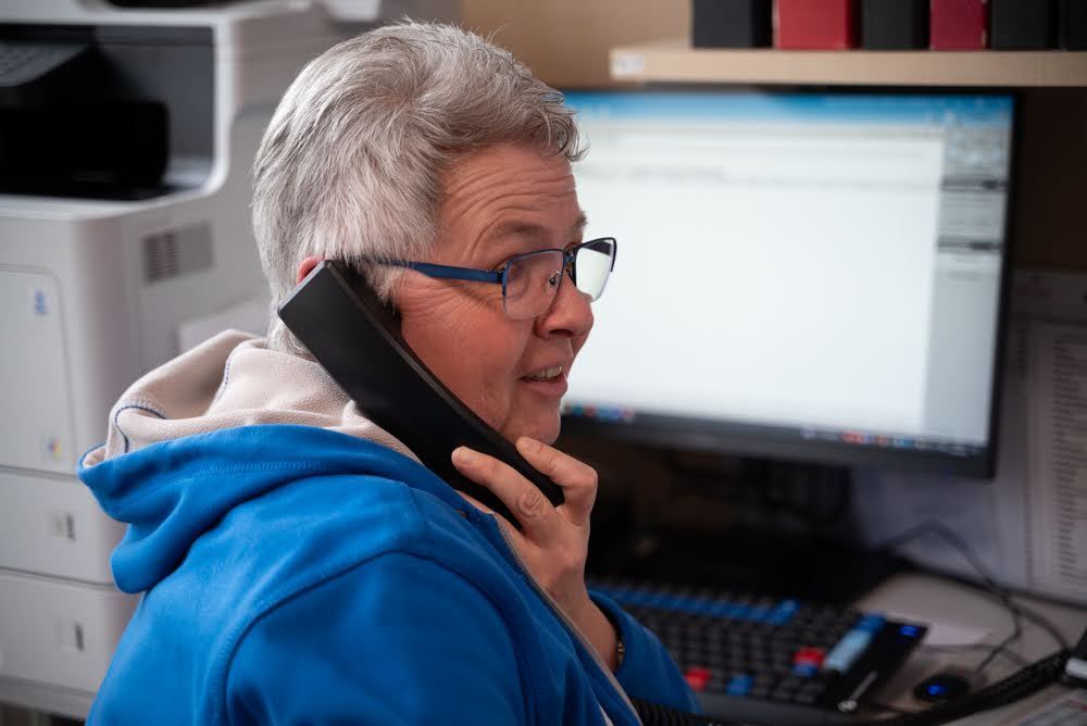 Eine Frau in einem blauen Kapuzenpullover telefoniert vor einem Computer