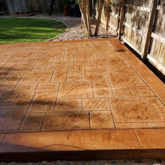 Stamped concrete patio with brown stone pattern and border, next to a fence and grass.