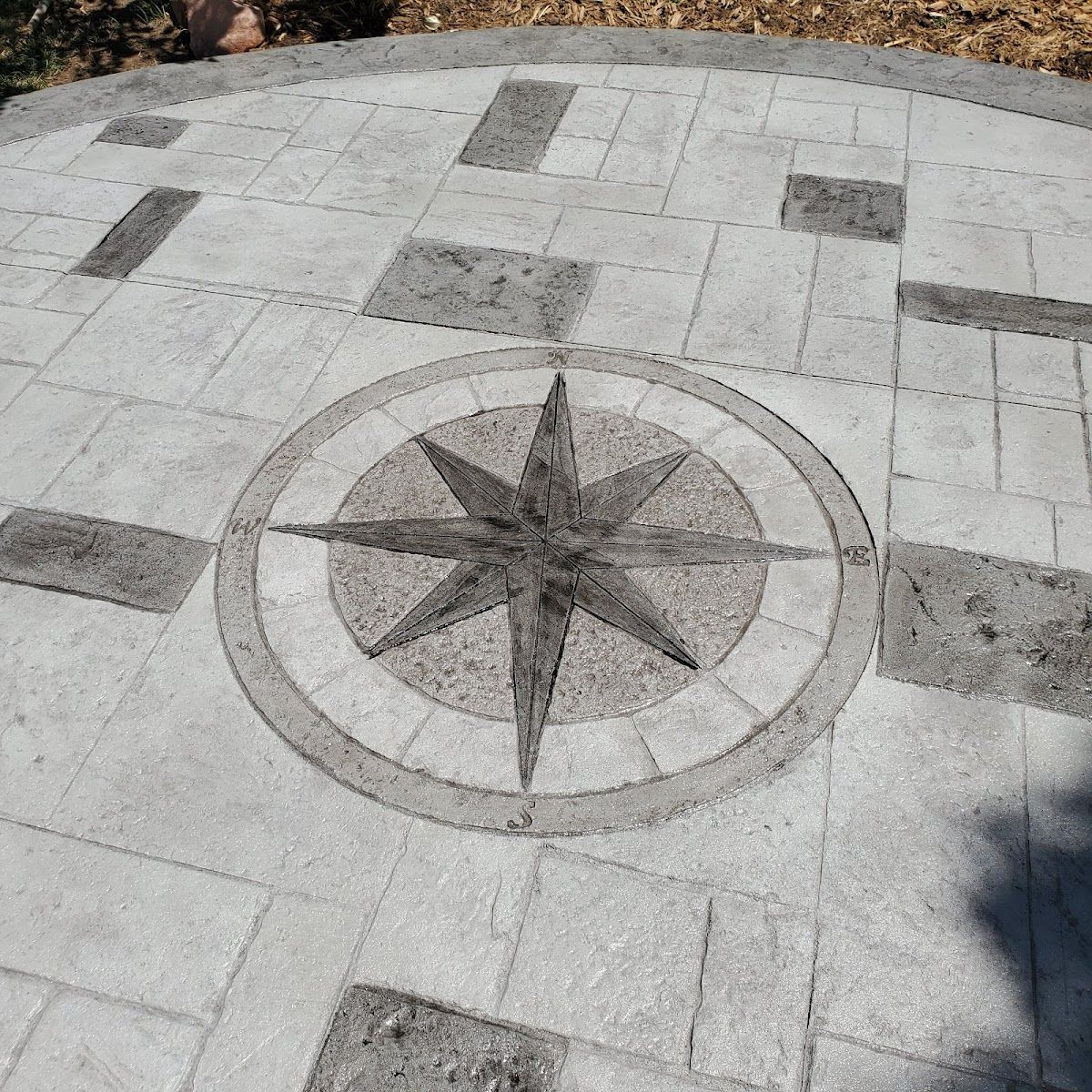 Circular paved patio with a compass rose design in the center, surrounded by rectangular stones.