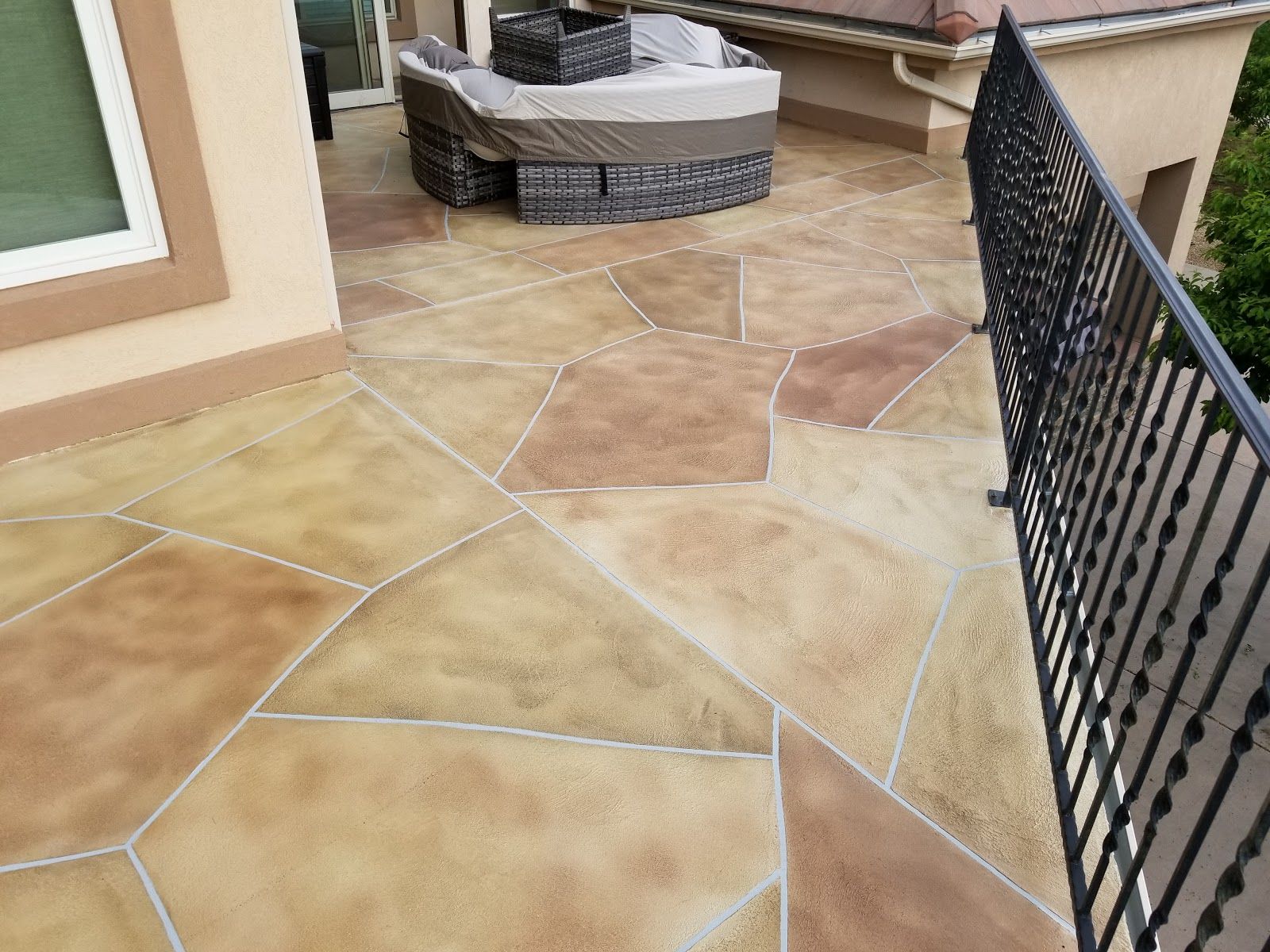 Stone-look patio with tan and brown sections, a black railing, and outdoor furniture.