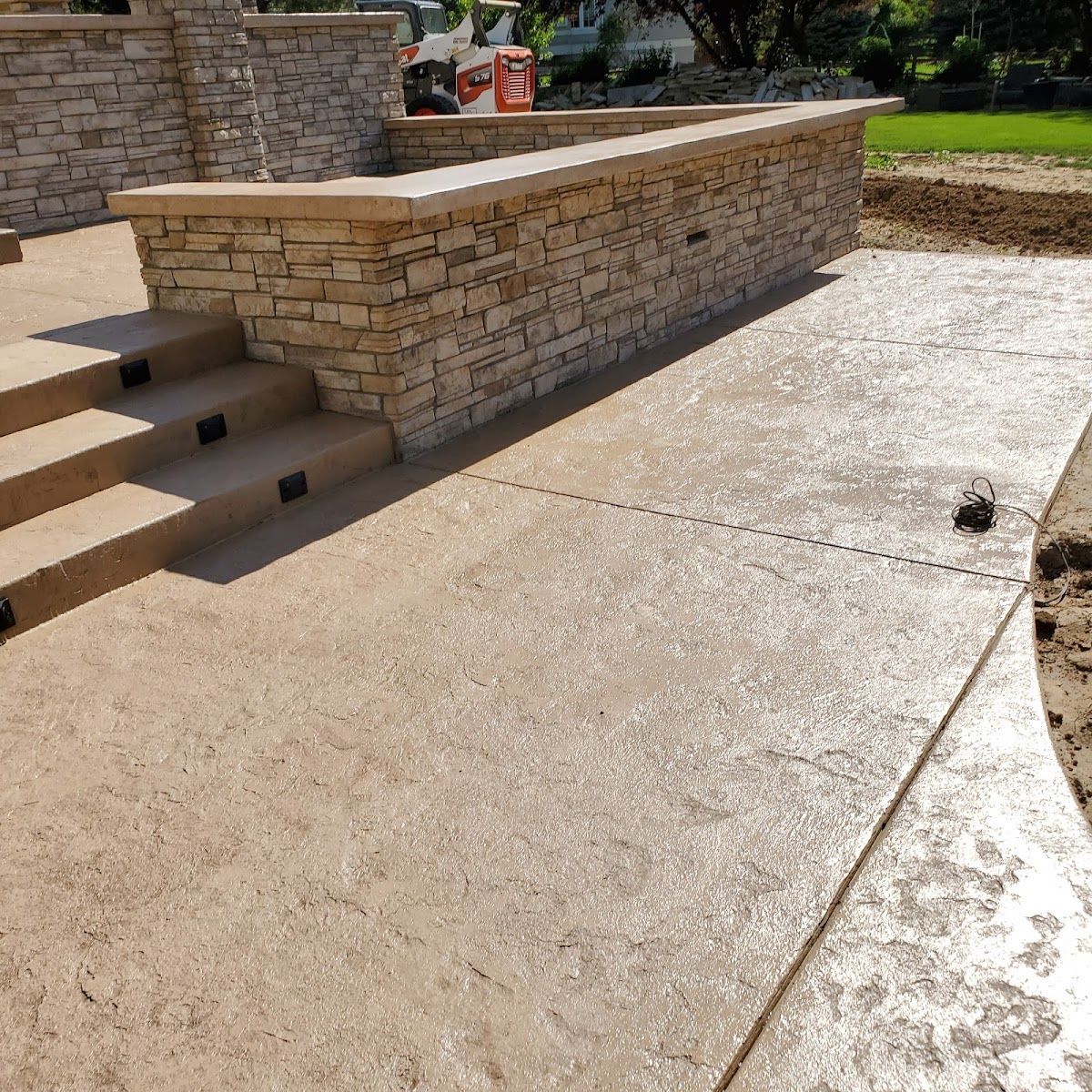 Stone patio with steps and textured concrete walkway, a raised stone wall.