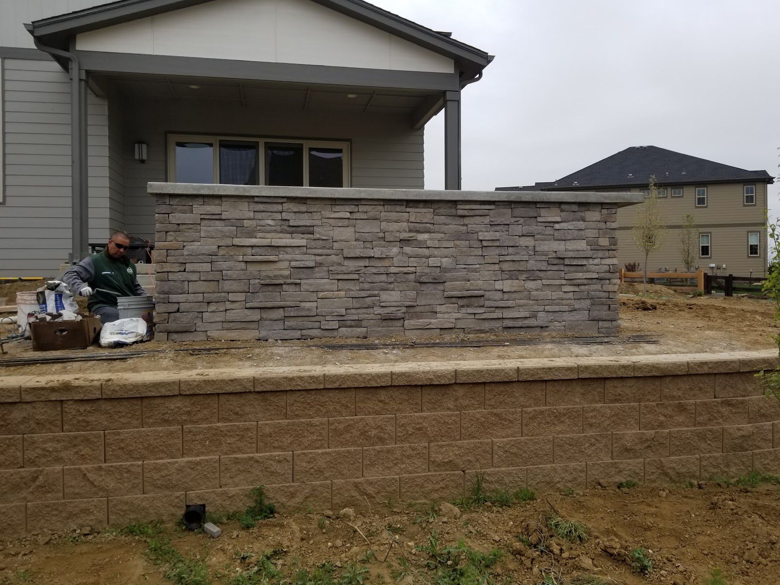 Stone-clad retaining wall next to a house under construction; a worker is present.