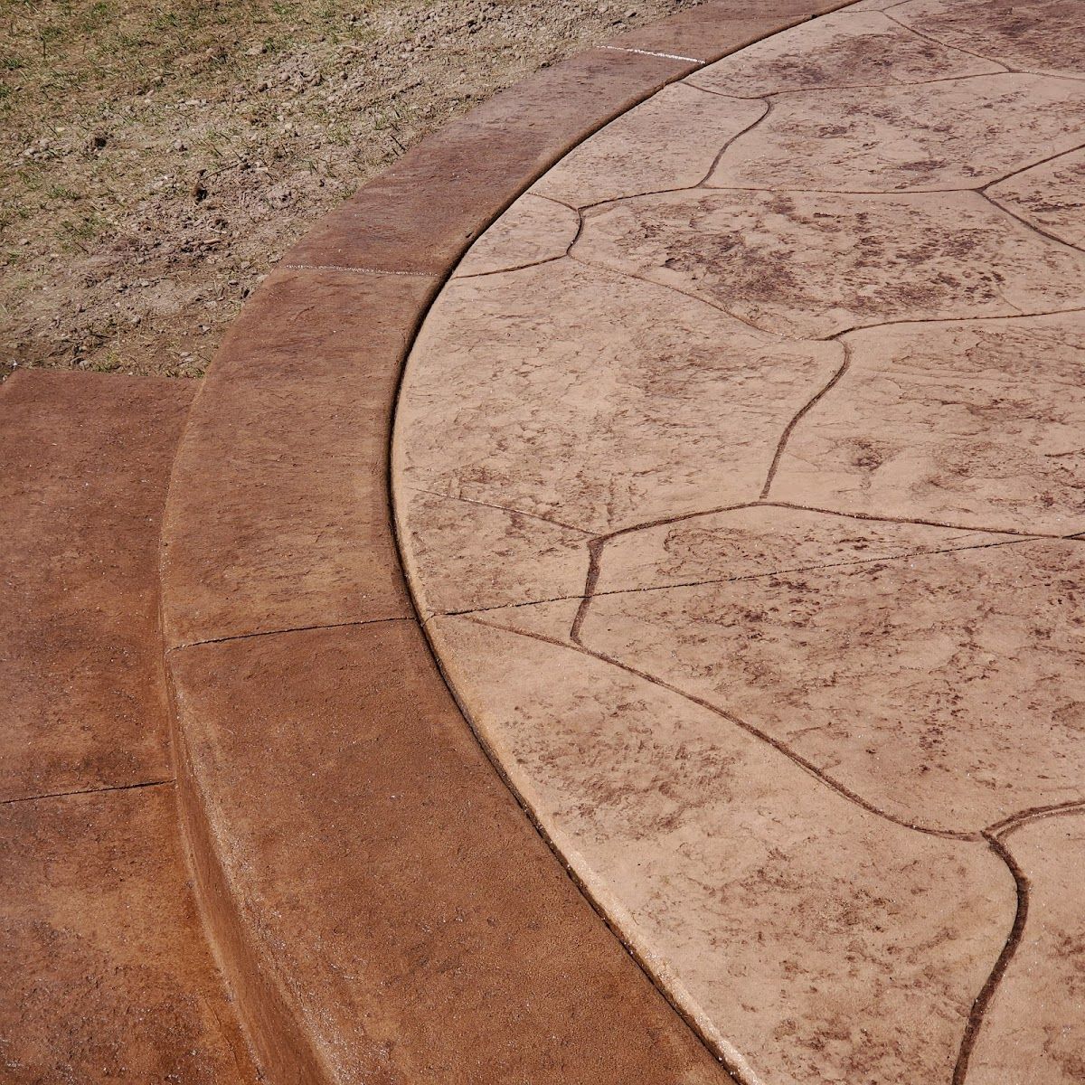 Brown stamped concrete patio with curved border, next to grass.