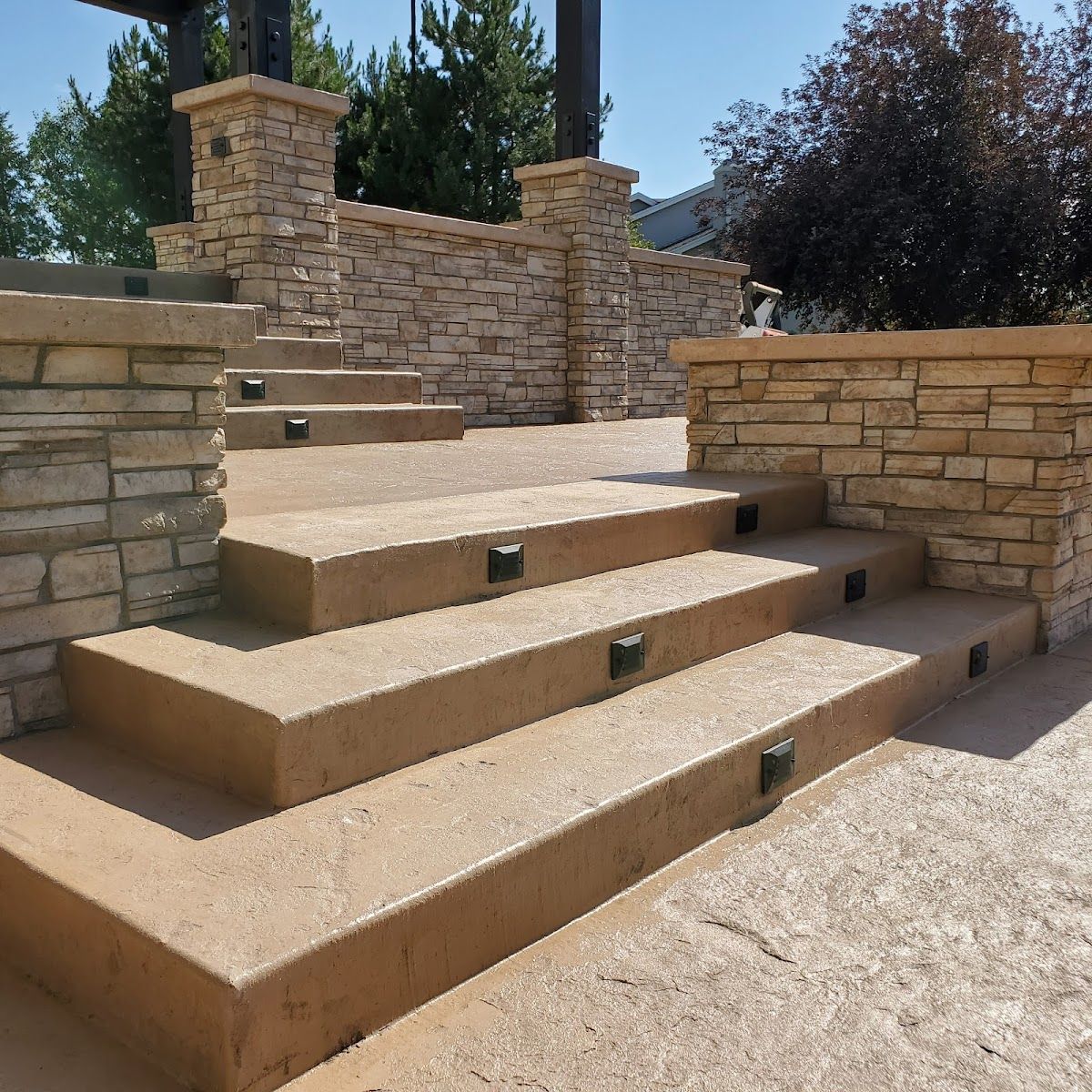 Stone steps leading up to a stone wall, lit by small square lights. Sunny outdoor setting.