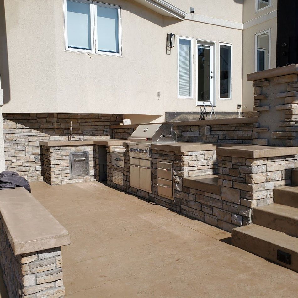 Outdoor kitchen with stone facing, concrete countertops, stainless steel grill, and steps.