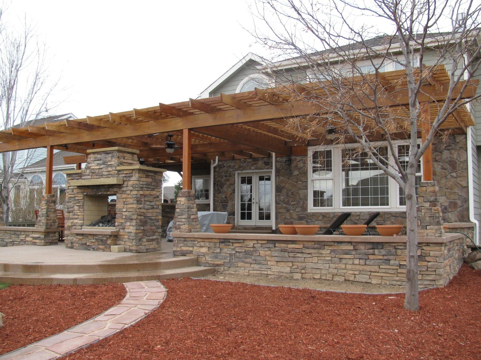 Stone patio with pergola, fireplace, and house; pathway in red mulch.