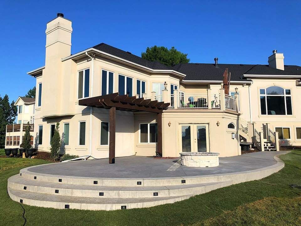 Beige house with patio and pergola, on a lawn. Steps lead up to the patio area. Blue sky.