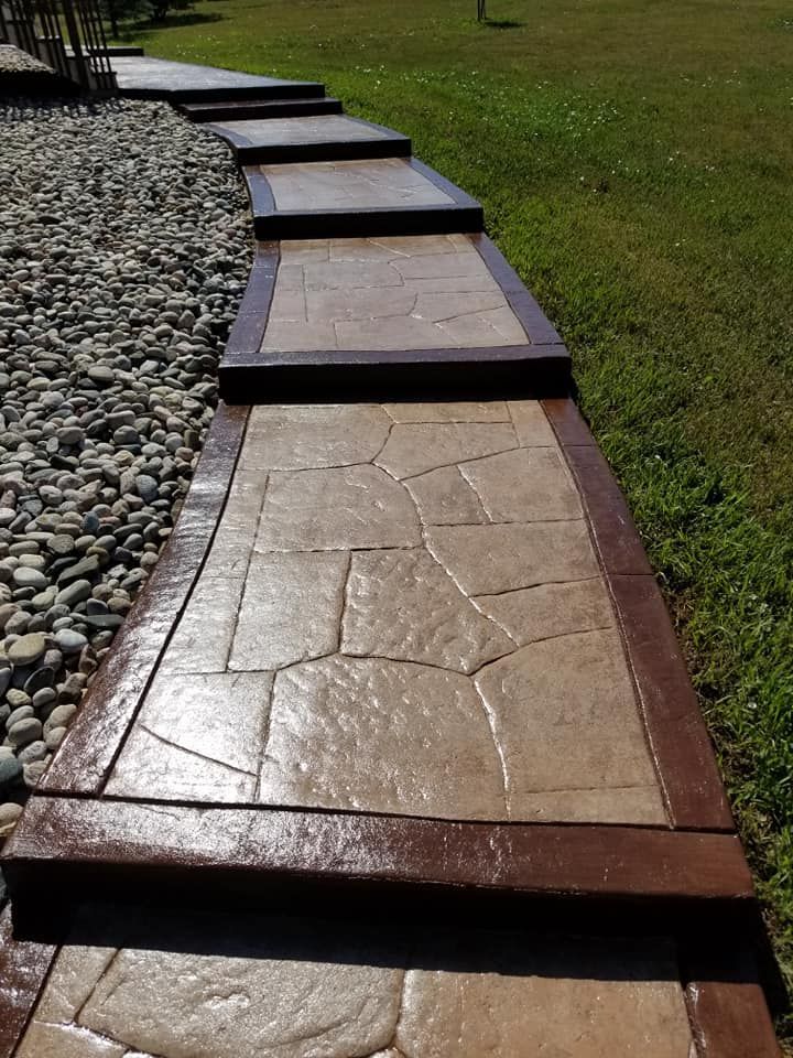 Stone pathway with dark brown borders and tan stone pattern, beside a green lawn.