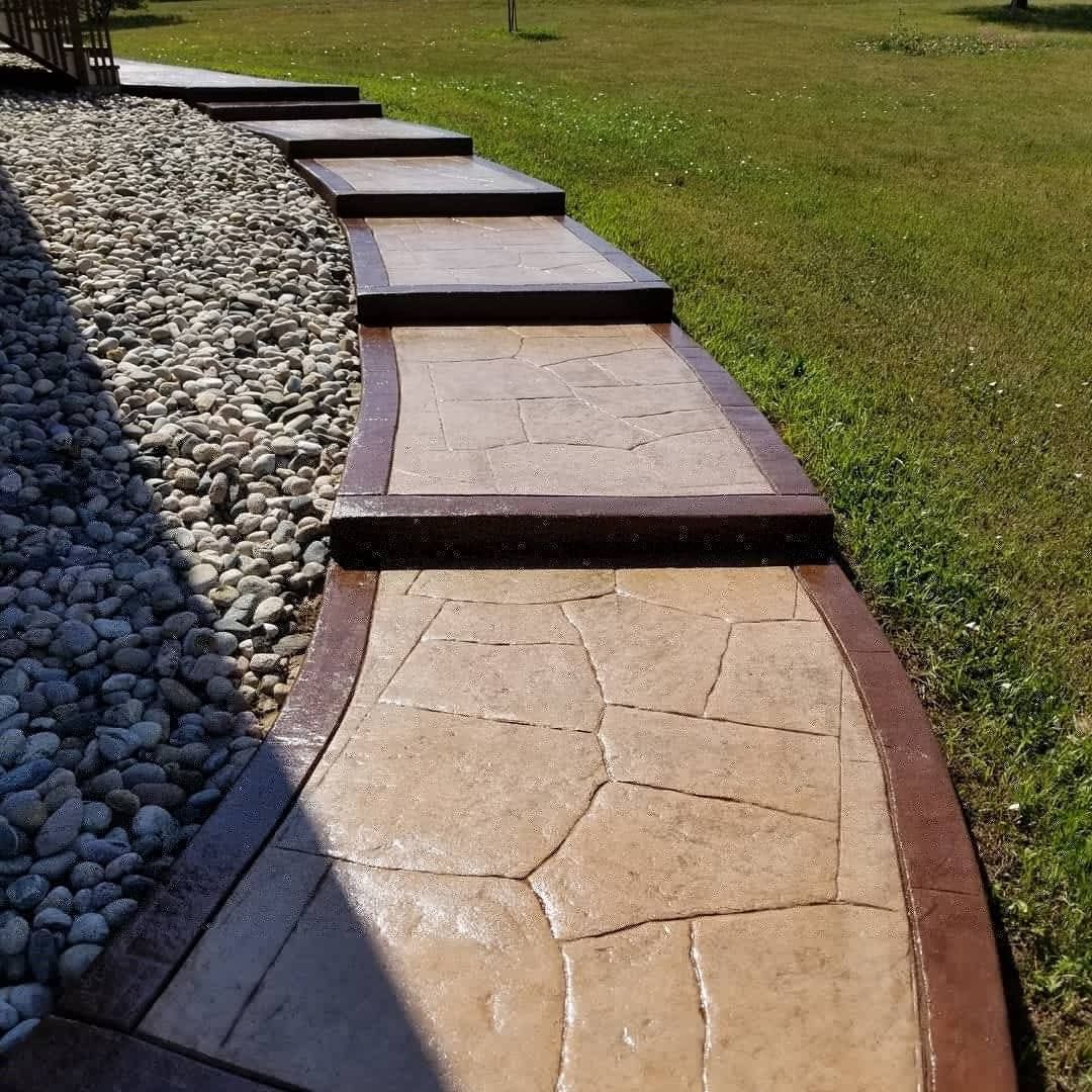 Stone path with brown borders and steps, beside a gravel and grass area.