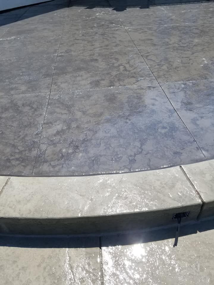 Gray stamped concrete patio with a curved edge and step.