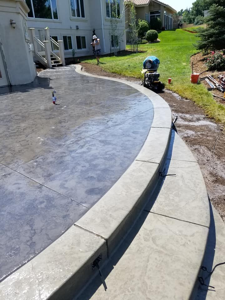 Newly poured gray concrete patio with curved steps, next to a grassy lawn, with a house in the background.