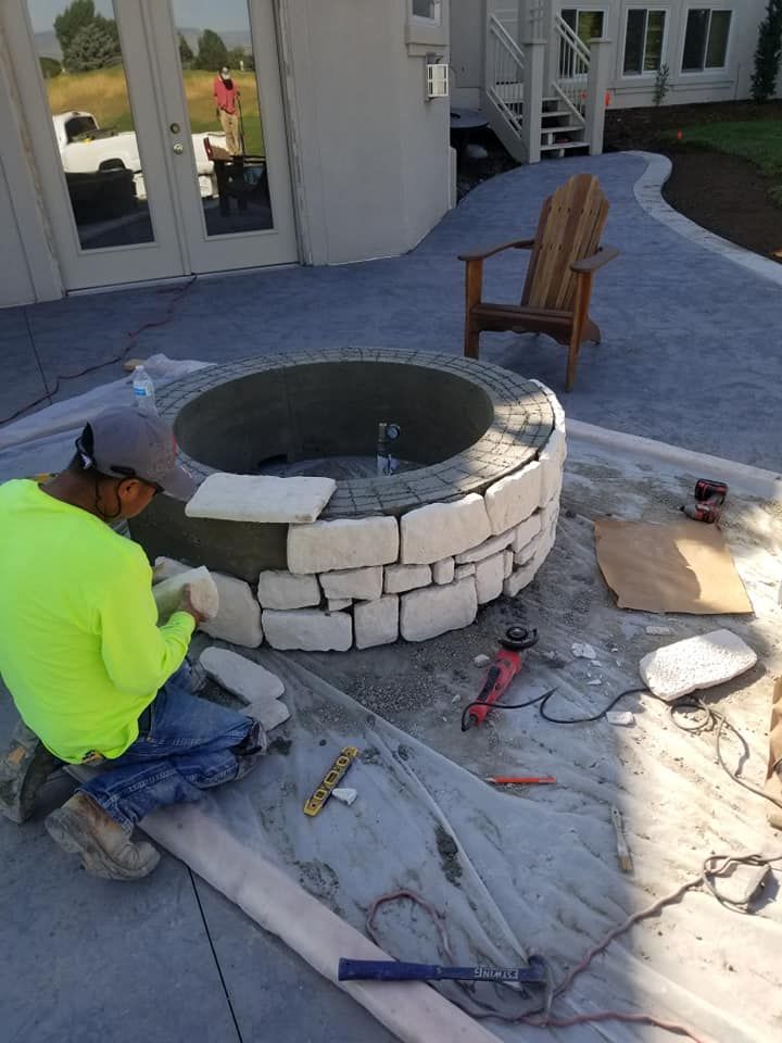 Man installing stone on a fire pit on a patio.