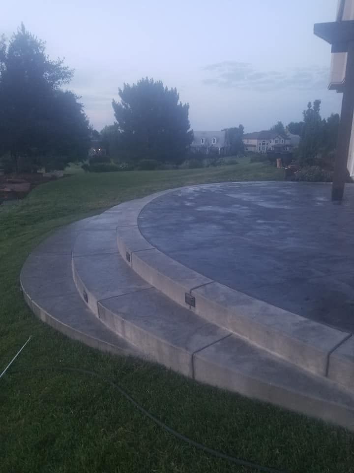 Concrete patio with curved steps leading onto a grassy lawn, a cloudy sky in the background.