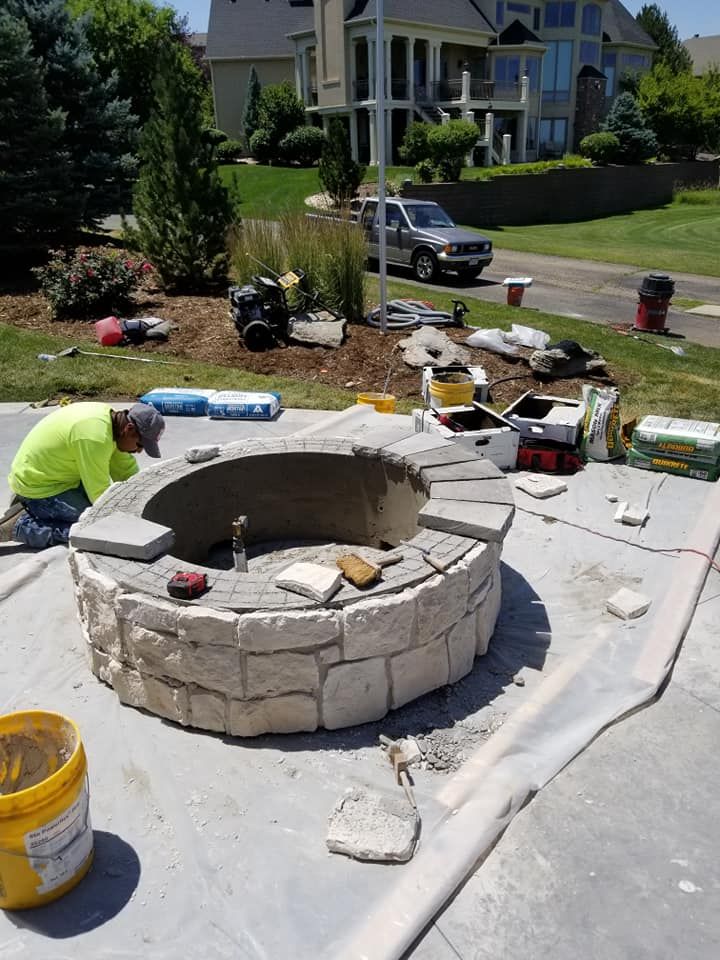Person in neon shirt building a stone fire pit on a concrete patio.