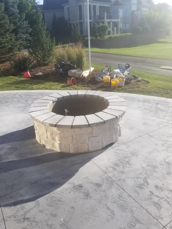 A stone fire pit on a concrete patio in front of a house, with construction supplies in the background.